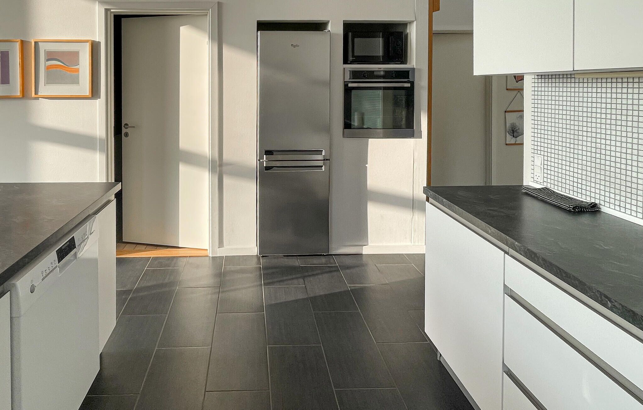 Una cocina moderna con refrigerador de acero inoxidable, microondas integrado, horno y salpicadero de azulejos.