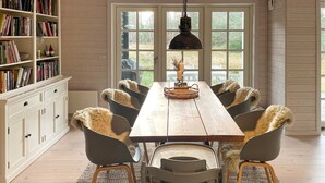 A dining room with a wooden table, six chairs with fur throws, a hanging light fixture, and a bookshelf filled with books. - Stunning home in Højby with WiFi (Højby)
