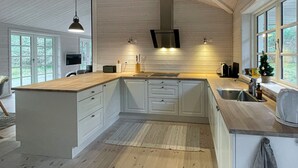 A modern kitchen with white cabinets, a wooden countertop, and a large island. There is a window with a view of trees, and a small Christmas tree on the counter. - Stunning home in Højby with WiFi (Højby)