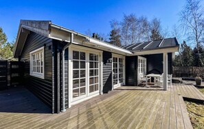 Ein Haus mit einer Terrasse, einem Kamin und einer überdachten Sitzgruppe im Freien.