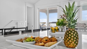 Une cuisine avec une table à manger dressée pour le petit-déjeuner, où l’on trouve des viennoiseries, des fruits et un ananas.