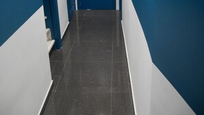 Ein Korridor mit blauen Türen und weißen Wänden, der zu einer geschlossenen Tür am Ende führt.