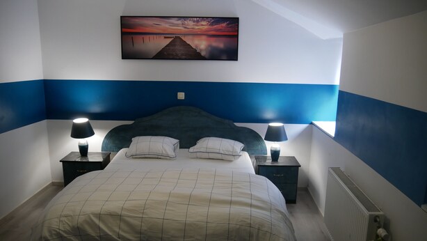 Ein Schlafzimmer mit einem Bett, zwei Nachttischen mit Lampen, einem zusätzlichen Tisch, einem Heizkörper und einem Wandbild.