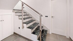 Eine Treppe mit Marmorstufen und einem Metallgeländer, die zu einer weißen Tür führt.