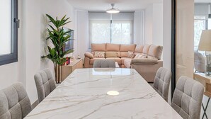 Ein modernes Wohnzimmer mit einem beigen Sofa, einem Glastisch und einem großen Fenster.
