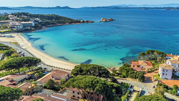 A coastal town with a beach, clear blue waters, and residential buildings.