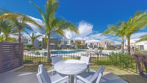 Ein Poolbereich mit Tisch und Stühlen, Palmen und modernen Gebäuden im Hintergrund.