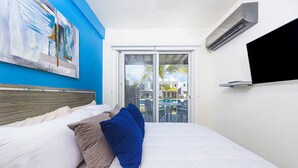 Ein Schlafzimmer mit Bett, einem Bild an der Wand und Blick auf einen Pool und Gebäude durch eine Schiebetür.