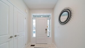 Un couloir avec une porte blanche, un tapis noir et un miroir décoratif en métal accroché au mur.