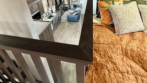 Een slaapkamer in loft-stijl met uitzicht op de keuken en woonruimte, houten balken en een groot raam.