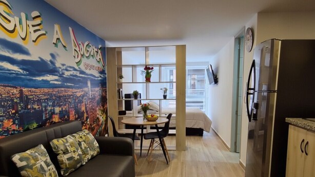 A modern apartment with a living room featuring a black sofa and patterned cushions, a dining area with a white table and chairs, and a kitchen with a stainless steel refrigerator. - Centro Historico de Bogotá, Apartment inTorre Ventto art and relaxation (Bogota)