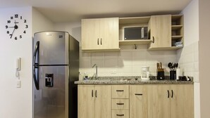 A compact kitchen with a stainless steel refrigerator, wooden cabinets, a microwave, and a coffee maker. - Centro Historico de Bogotá, Apartment inTorre Ventto art and relaxation (Bogota)