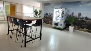 A modern indoor space with a long table and chairs, a vending machine, and a mural of a cityscape. - Centro Historico de Bogotá, Apartment inTorre Ventto art and relaxation (Bogota)