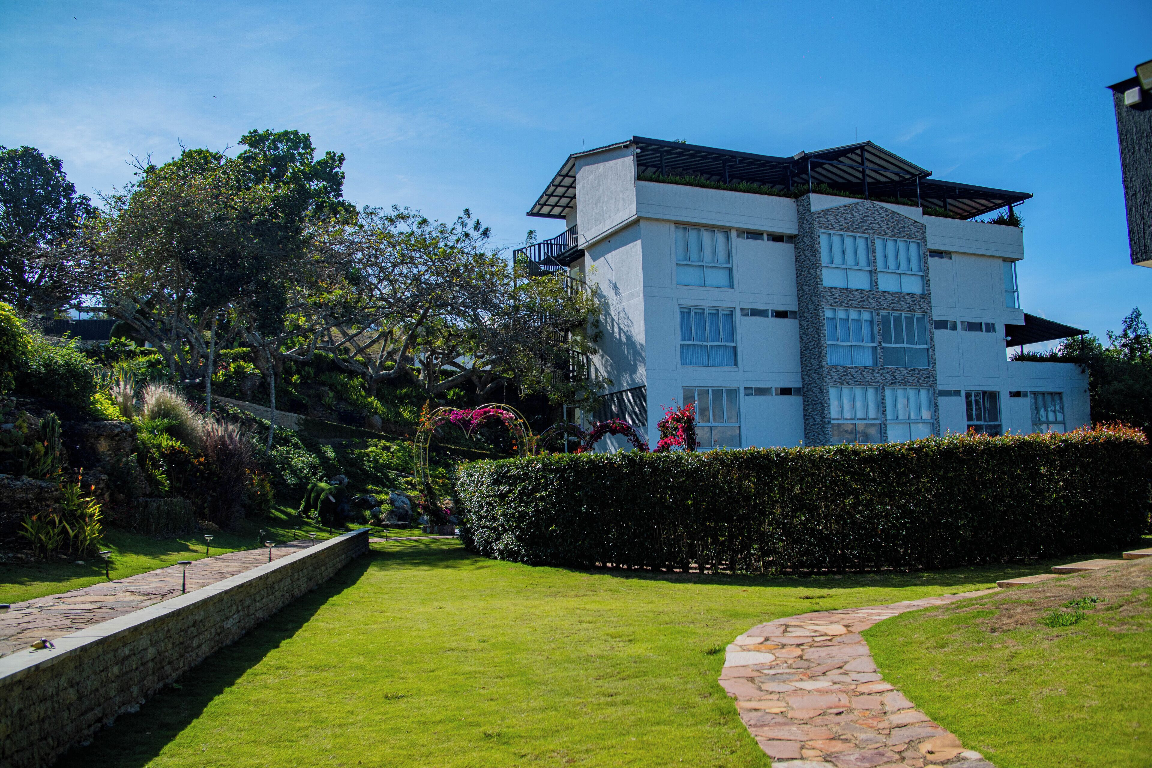 Un edificio moderno de varios pisos con fachada de piedra, ventanas grandes y un jardín en la azotea.
