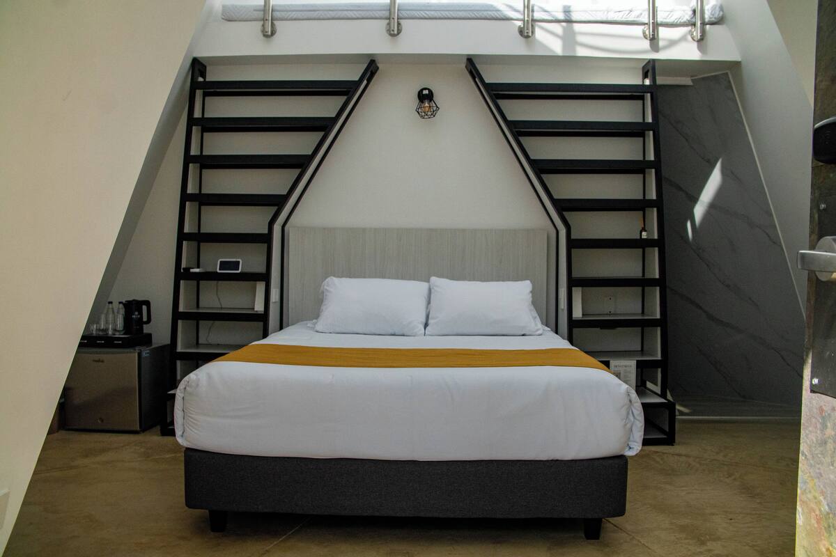 A modern bedroom with a bed, a nightstand, a coffee maker, and a shelf unit.