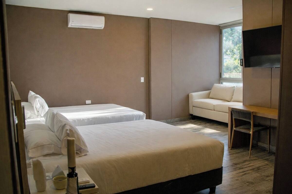 A hotel room with two beds, a sofa, a desk, and a TV.