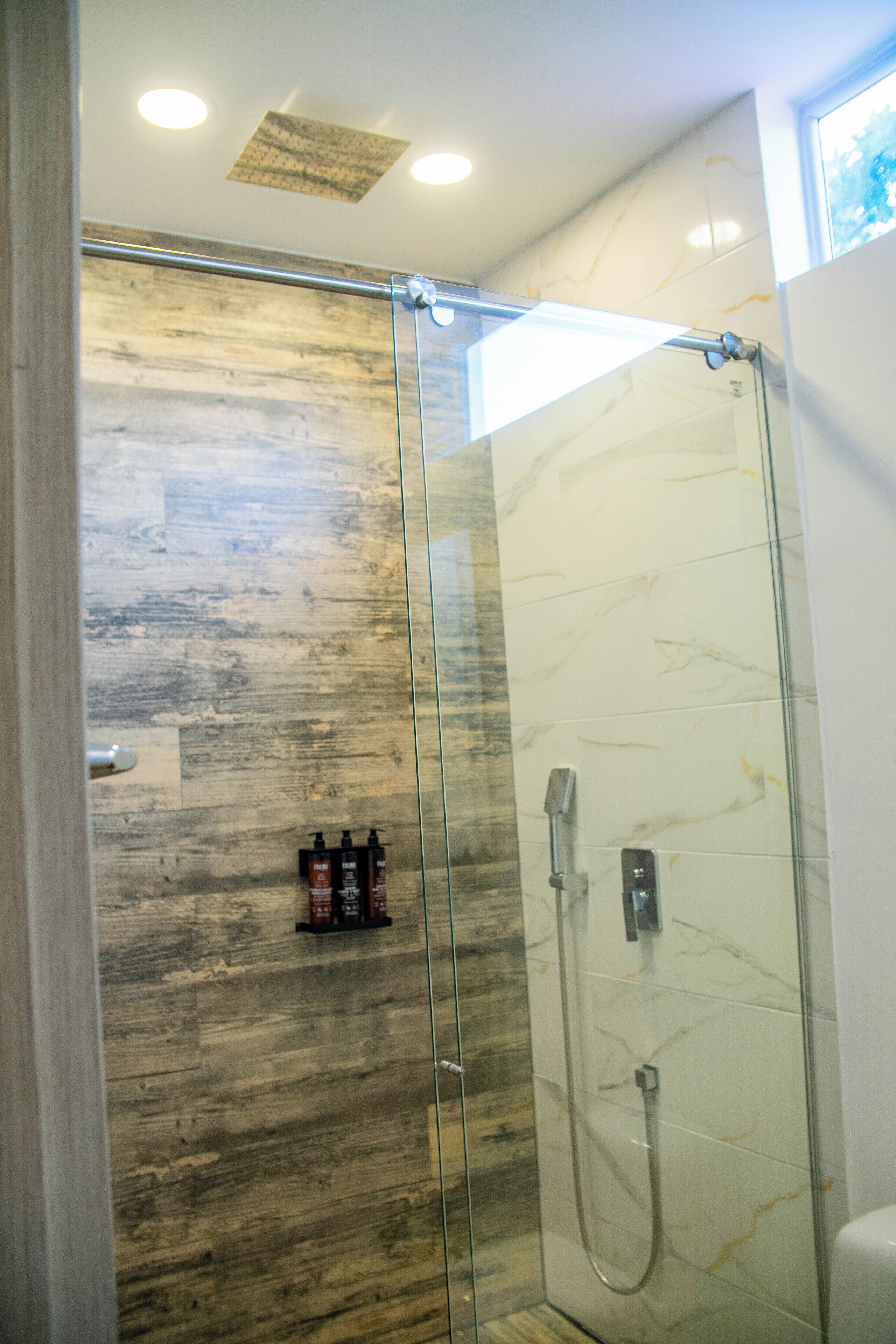 Una cabina doccia in vetro con parete in legno e rivestimento in marmo.