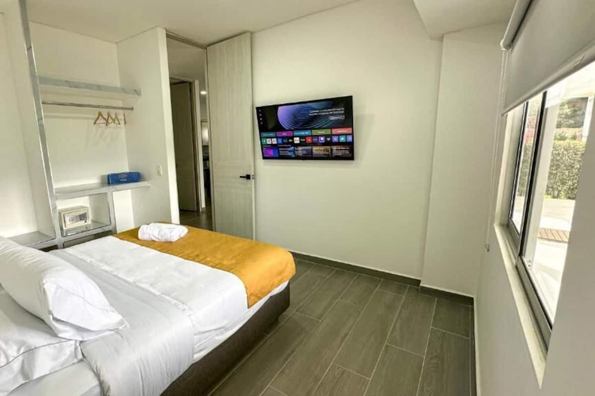 A modern hotel room with a bed, a TV mounted on the wall, and a window.