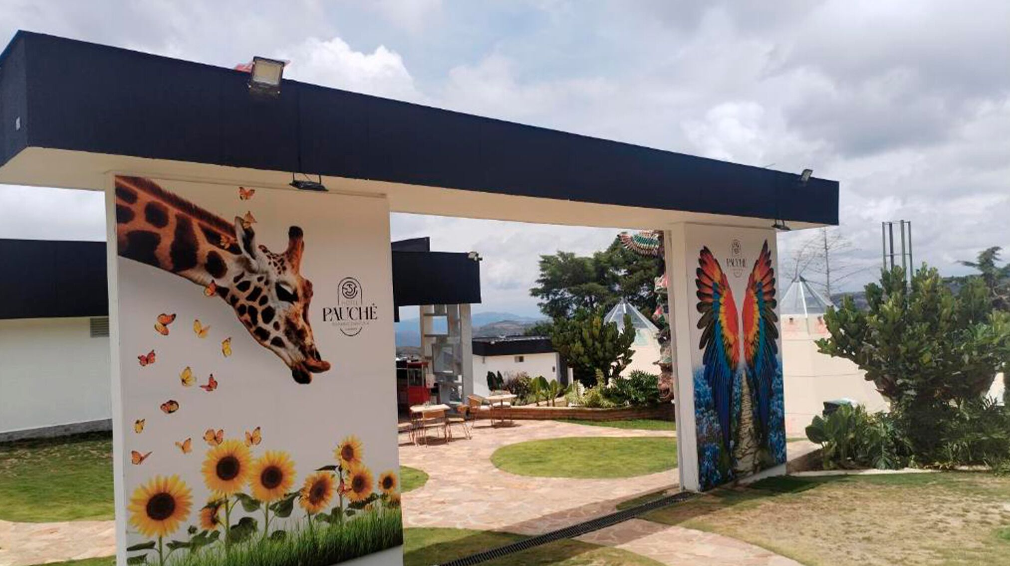A hotel entrance with a giraffe mural, sunflowers, and a parrot wing mural.