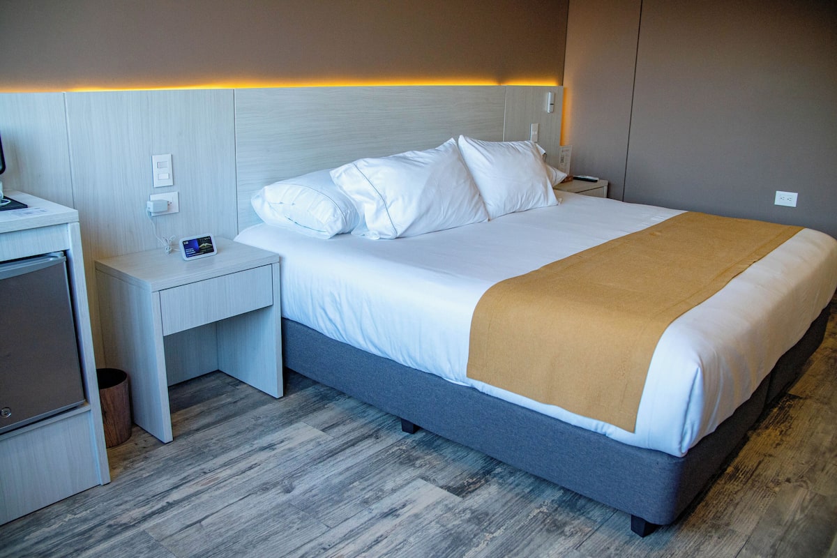 A modern hotel room with a bed, bedside table, and a small desk with a chair.
