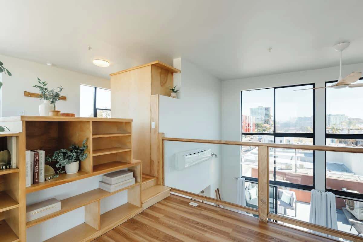 Un appartement moderne doté d’un escalier en bois, d’une bibliothèque intégrée et de grandes fenêtres offrant une vue sur la ville.