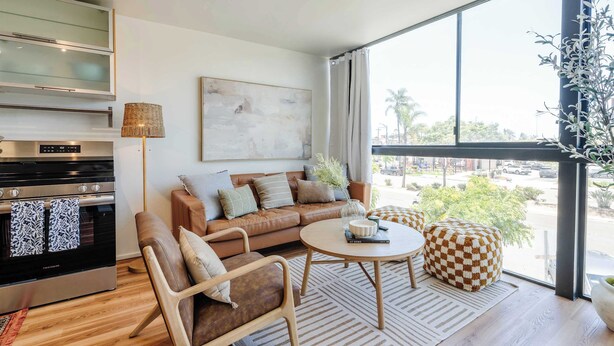 A modern living room with a sofa, coffee table, and a view of the street through large windows. - Hillcrest Hideaway – Stylish Loft in the Heart of SD (San Diego)