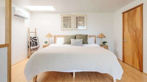 A bedroom with a bed, two bedside lamps, a wooden wardrobe, a small bedside table with a lamp, and a wall-mounted air conditioner. - Hillcrest Hideaway – Stylish Loft in the Heart of SD (San Diego)