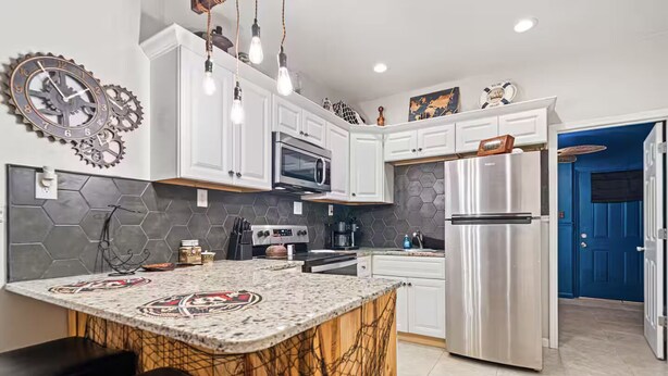 A modern kitchen with white cabinets, a stainless steel refrigerator, a microwave, and a coffee machine.