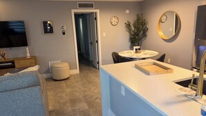 Uma cozinha moderna com uma ilha central, uma sala de jantar com mesa redonda e uma sala de estar com televisão de tela plana.