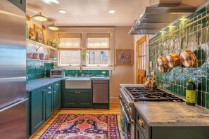 A kitchen with teal cabinets, a gas stove, a microwave, and a sink. - Luxe Historic West End • Walk to Downtown • Near Wake Forest • 2BDRM (Winston-Salem)