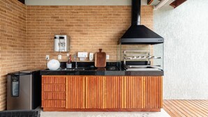 A compact kitchen with a brick wall, a black range hood, a built-in oven, and a wooden countertop. - Houses in Gated Community With Pool and BBQ Area - PCR (Porto Seguro)