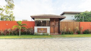 A residential property named "Pina Carneiro" with a paved entrance, a wooden gate, and a red wall. - Houses in Gated Community With Pool and BBQ Area - PCR (Porto Seguro)