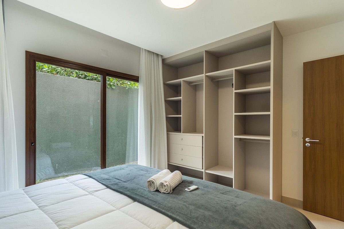 A modern bedroom with a bed, a walk-in closet, and a sliding glass door to a balcony.