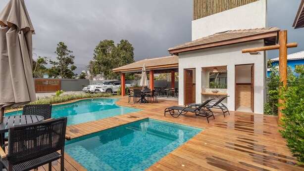 A swimming pool with lounge chairs and a covered patio area. - Houses in Gated Community With Pool and BBQ Area - PCR (Porto Seguro)