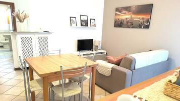 Un salon moderne avec une table à manger en bois, deux chaises, un canapé et un téléviseur.