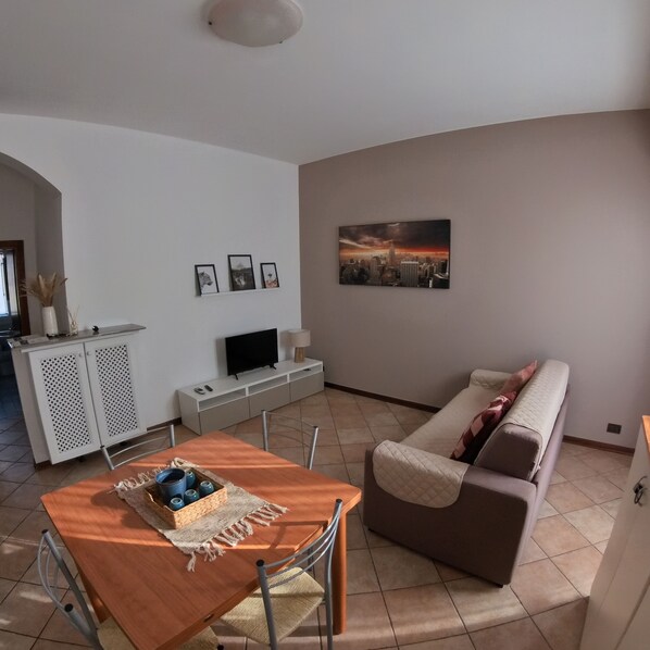A living room with a sofa, a TV, a dining table, and a painting on the wall. - Città di Brescia adorable 4 person apartment with AC in Brescia Hospital Area (Brescia)