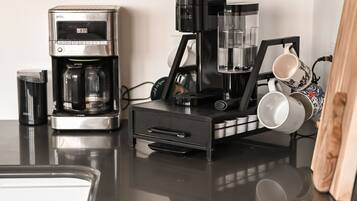 Une cuisine équipée d’une machine à café, d’une bouilloire et d’un moulin à café, le tout posé sur le plan de travail.