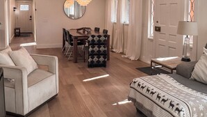 Un salon moderne comprenant un canapé, une table à manger avec des chaises, un lustre et une grande fenêtre avec des rideaux.
