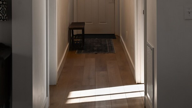 Un couloir avec une porte blanche, un petit banc et une fenêtre donnant sur l’extérieur.