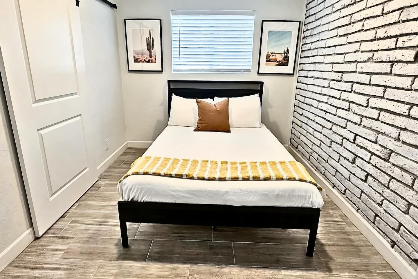 A bedroom with a bed, a brick wall, and two framed pictures on the wall.