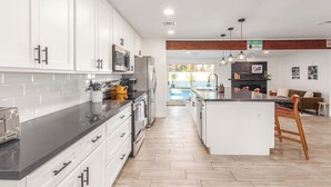Uma cozinha moderna com armários brancos, uma ilha central e uma área de jantar com sofá e cadeiras.