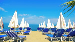 A beach with rows of blue and white beach chairs and umbrellas, a clear blue sky, and the ocean in the background. - FAFA Mel Holiday Hotel (Golem)