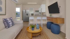 Un ambiente compatto con divano, tavolino e oggetti decorativi, televisore a parete e angolo cottura con frigorifero e sedie.