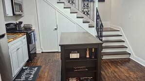 A modern kitchen with white cabinets, a microwave, and a stove. A wooden dining table is in the center. - Spacious 4-bedroom house in New Orleans with AC (New Orleans)