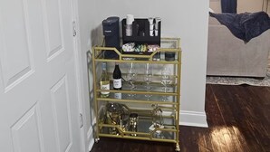 A room with a white door, a glass display cabinet with wine glasses and bottles, a ceiling fan, and a bed with a blue blanket. - Spacious 4-bedroom house in New Orleans with AC (New Orleans)