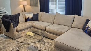 A living room with a sectional sofa, a glass coffee table, a ceiling fan, a lamp, and a window with curtains. - Spacious 4-bedroom house in New Orleans with AC (New Orleans)