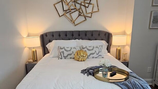 A bedroom with a tufted headboard, a round bedside table, a bed with a white and gray duvet, and a ceiling fan. - Spacious 4-bedroom house in New Orleans with AC (New Orleans)
