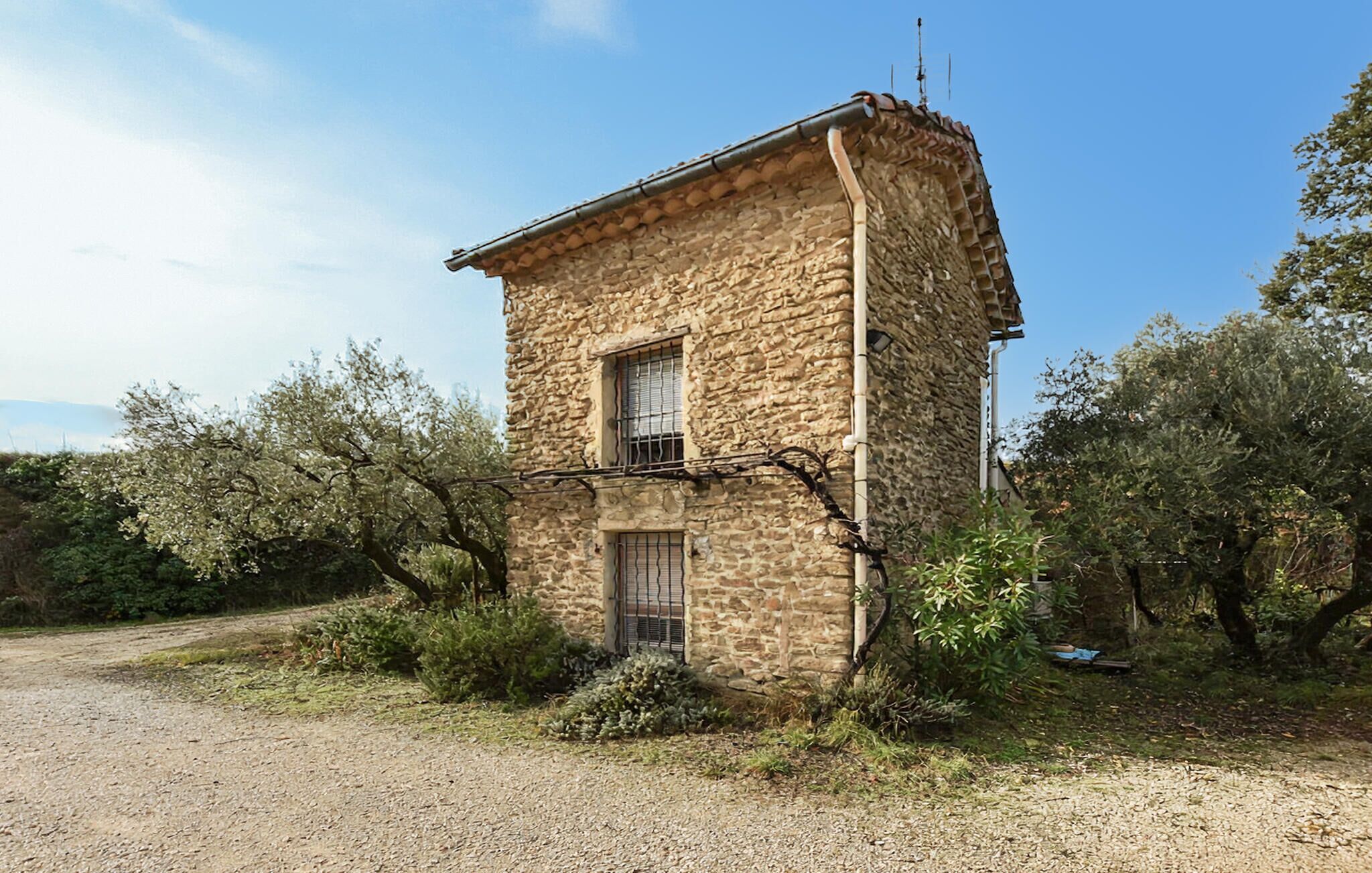 Ein Steinhaus mit einem kleinen Fenster und einer Tür, umgeben von Bäumen und Sträuchern.