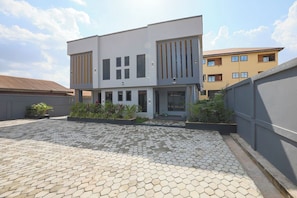 A modern two-story building with a flat roof, large windows, and a paved courtyard.