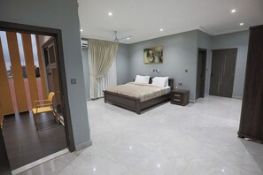 A modern bedroom with a large bed, a nightstand, a ceiling fan, and a door leading to another room.